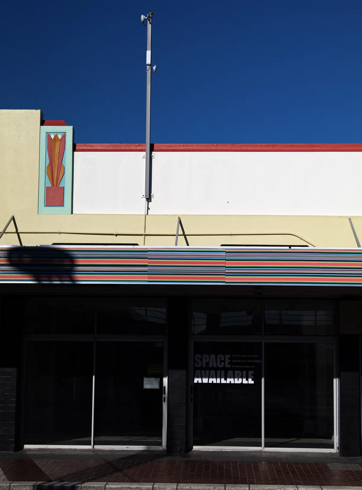 The six-metre Strip Painting along the fascia of the F.King building at 320 Heretaunga Street West, with the building's Art Deco panel and red parapet line above, under a deep blue sky