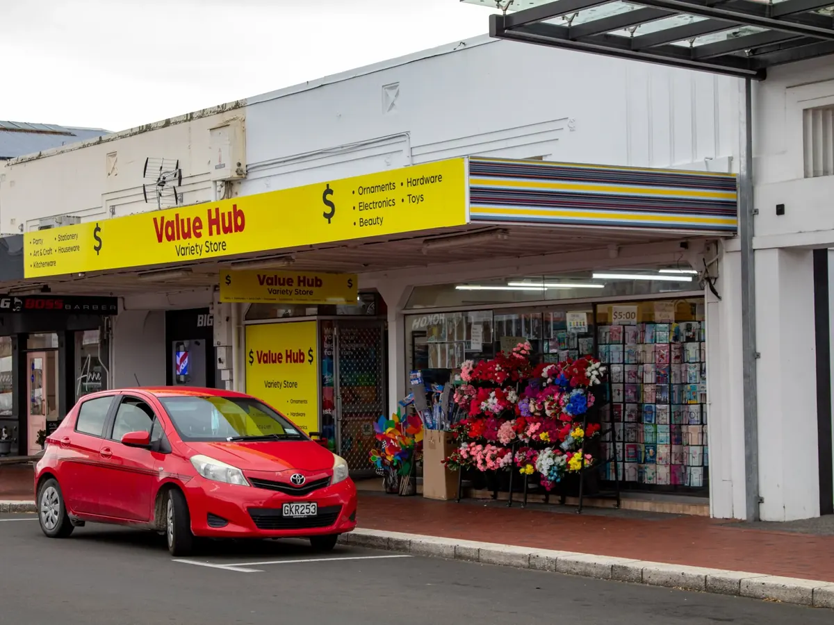 A Strip Painting of yellow, purple, slate and navy bands on the verandah fascia at 328 Heretaunga Street West, beside the yellow Value Hub Variety Store sign