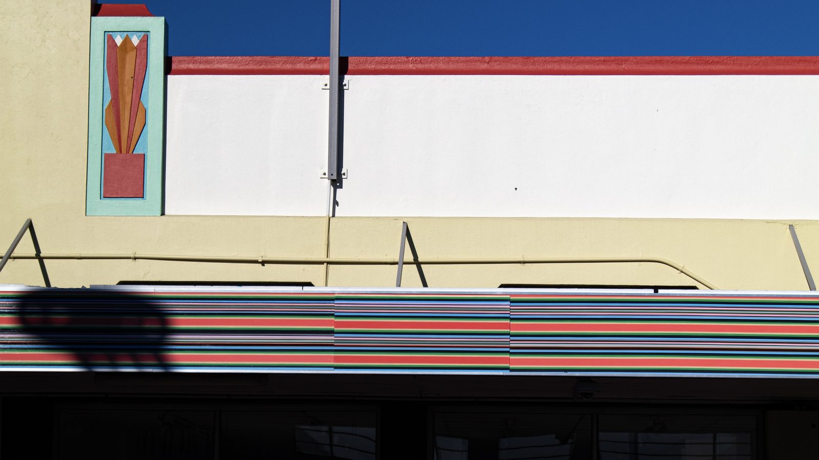 A long Strip Painting of coral, turquoise, green and blue bands along the fascia of the F.King building at 320 Heretaunga Street West, with the building's Art Deco panel and red parapet line above, under a deep blue sky